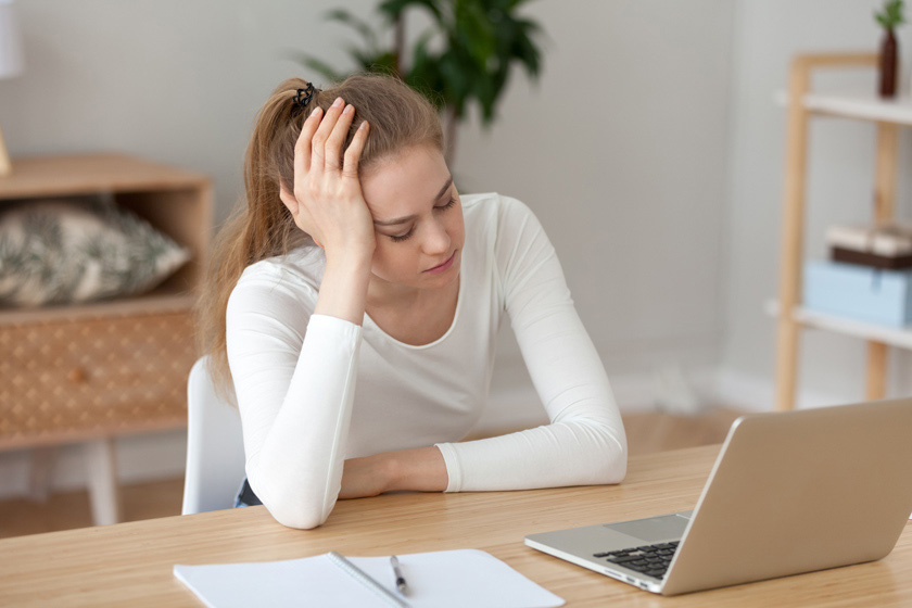 Грустная уставшая девушка сидит на стуле за столом с ноутбуком и блокнотом Девушка за ноутбуком