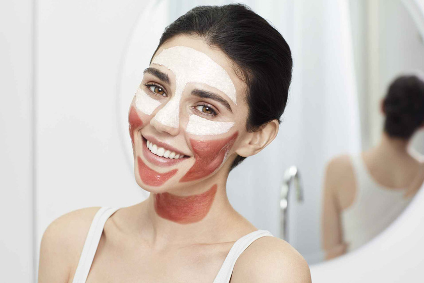 Девушка с масками, нанесенными в технике мультимаскинг, стоит спиной к зеркалу в ванной комнате Девушка с маской на лице